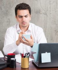 Office employee angrily looking his telephone at the office desk. High quality photo